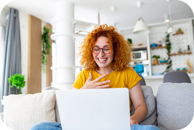 A smiling woman sitting on her couch with her laptop, enrolling in a plan at Your Health Idaho, Idah…