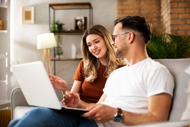 A young couple sitting on a couch with a laptop and reviewing about-us information on the Your Health Idaho website.