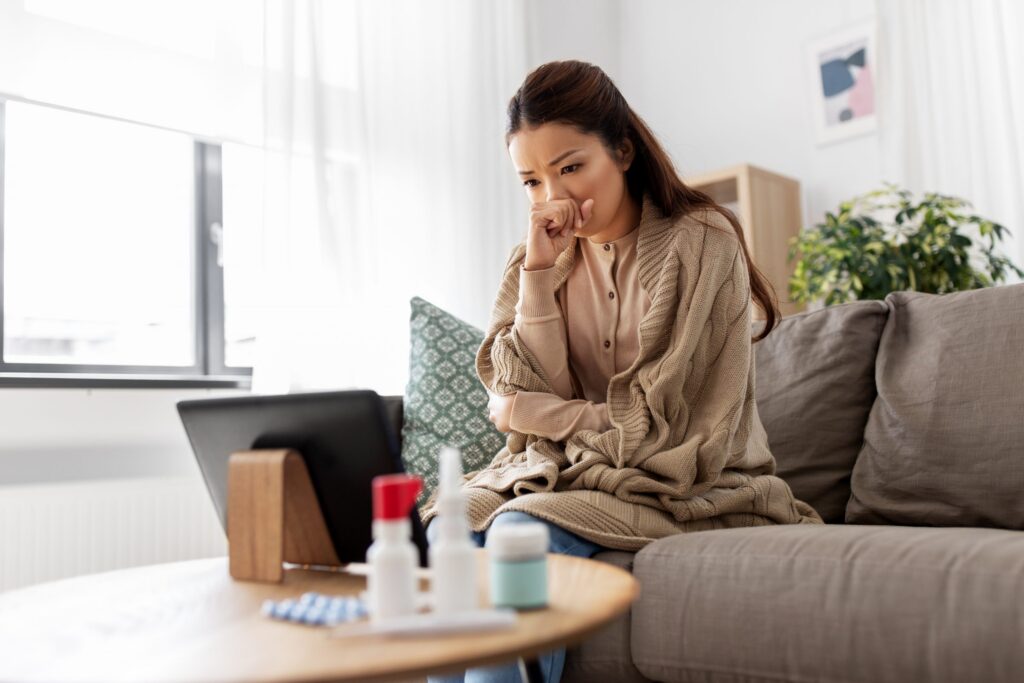 A woman sitting on her couch accessing telehealth on her computer to seek medical advice to treat her symptoms.